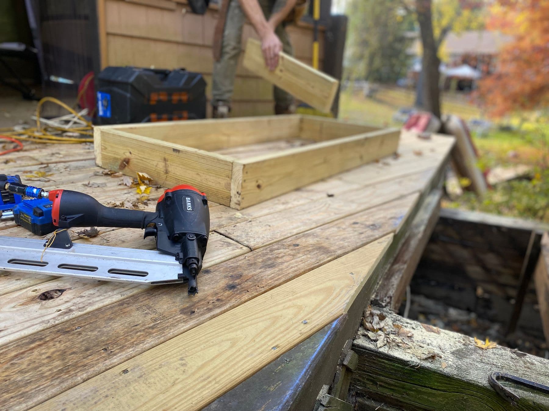 Carpenter fastening pressure-treated deck boards with a framing nailer during a backyard deck build
